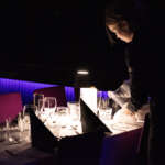 Mustapukuinen tarjoilija kaataa vettä katetun pöydän laseihin