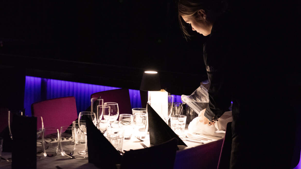 tarjoilija kaataa vettä illallispöydän laseihin show&dinner illassa