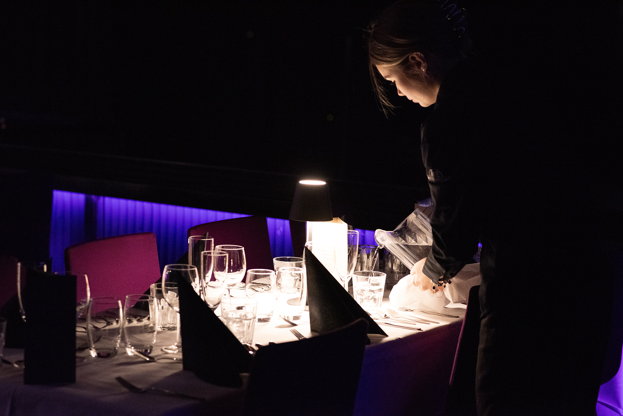 tarjoilija kaataa vettä illallispöydän laseihin show&dinner illassa